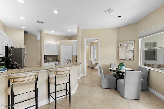 kitchen with light stone counters, visible vents, a peninsula, and white cabinets