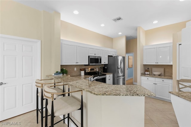 kitchen featuring visible vents, backsplash, a peninsula, a kitchen breakfast bar, and stainless steel appliances