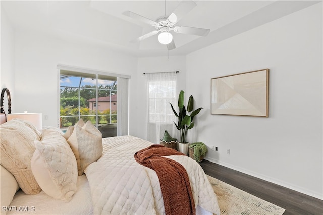 bedroom with ceiling fan, baseboards, a tray ceiling, and wood finished floors