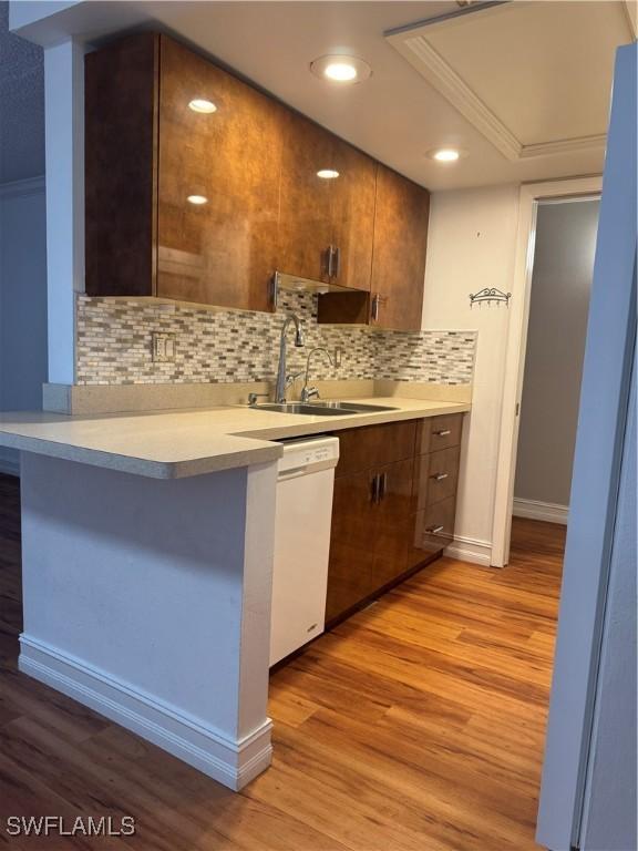 kitchen with light wood finished floors, light countertops, a sink, white dishwasher, and a peninsula