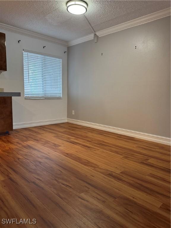 spare room with baseboards, a textured ceiling, ornamental molding, and wood finished floors