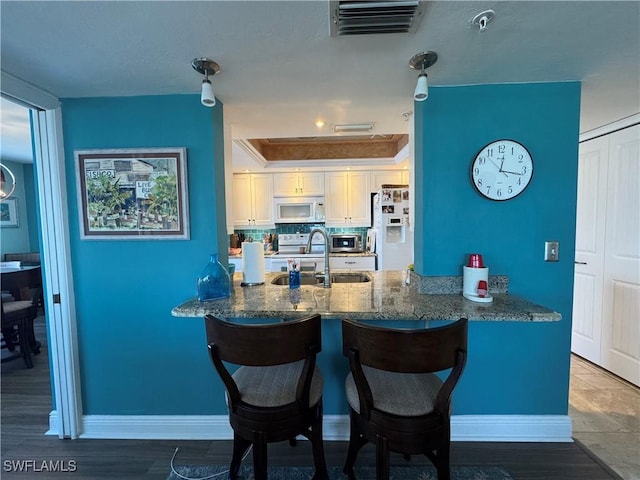 kitchen featuring sink, white appliances, white cabinetry, backsplash, and kitchen peninsula