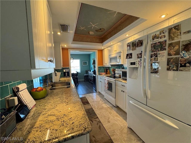 kitchen featuring tasteful backsplash, sink, white cabinets, a raised ceiling, and white appliances