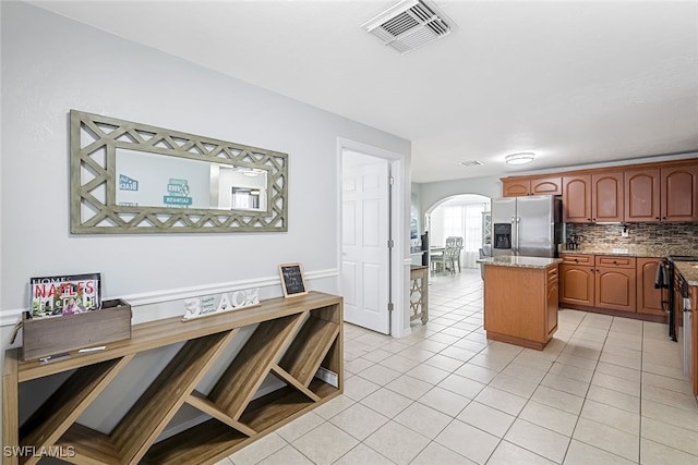 kitchen featuring light tile patterned floors, stainless steel fridge, light stone countertops, a kitchen island, and decorative backsplash