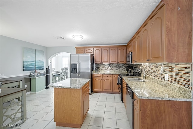 kitchen featuring backsplash, stainless steel appliances, a center island, light stone countertops, and light tile patterned flooring