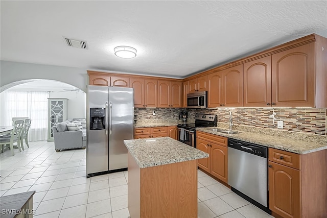 kitchen with light tile patterned floors, backsplash, stainless steel appliances, a center island, and light stone countertops