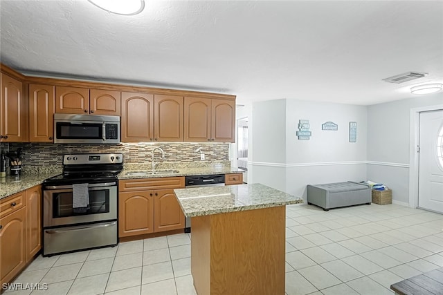 kitchen with light tile patterned flooring, appliances with stainless steel finishes, sink, a center island, and light stone counters