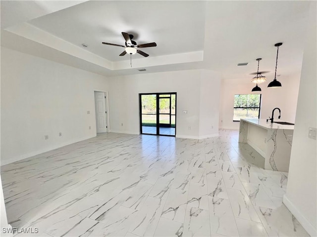 unfurnished room featuring sink, a wealth of natural light, a raised ceiling, and ceiling fan