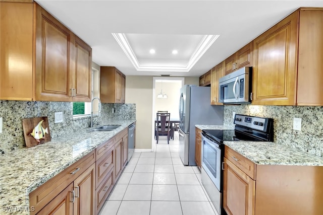 kitchen with sink, light tile patterned floors, appliances with stainless steel finishes, light stone counters, and a tray ceiling