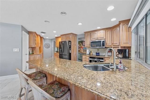 kitchen with a kitchen bar, sink, light stone counters, kitchen peninsula, and refrigerator with ice dispenser