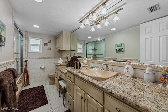 full bathroom featuring combined bath / shower with glass door, tile walls, vanity, toilet, and tile patterned floors