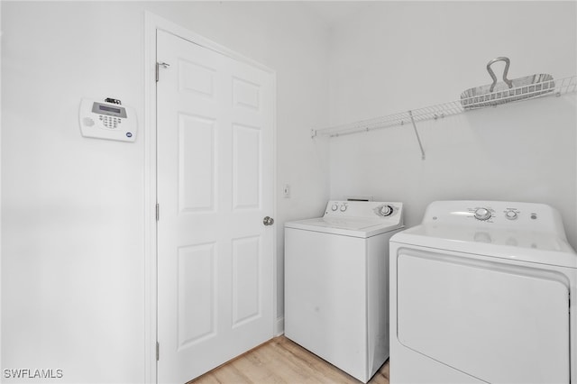 clothes washing area with washing machine and dryer and light hardwood / wood-style flooring