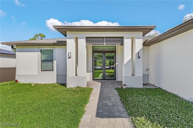 view of exterior entry featuring a lawn and french doors