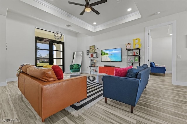 living room with ornamental molding, light wood-type flooring, ceiling fan, and a tray ceiling