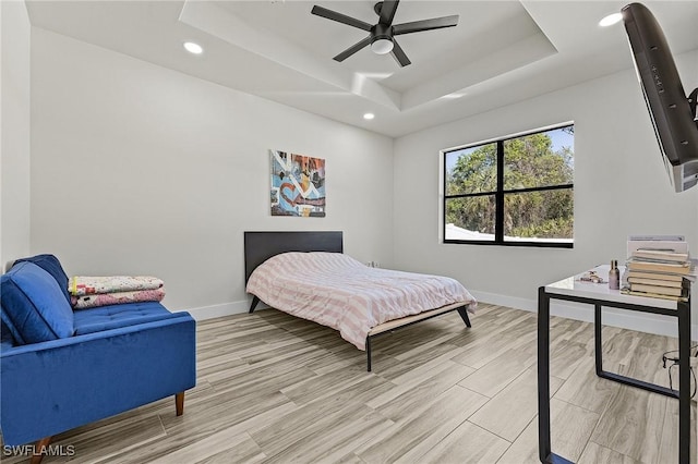 bedroom featuring ceiling fan, a raised ceiling, and light wood-type flooring