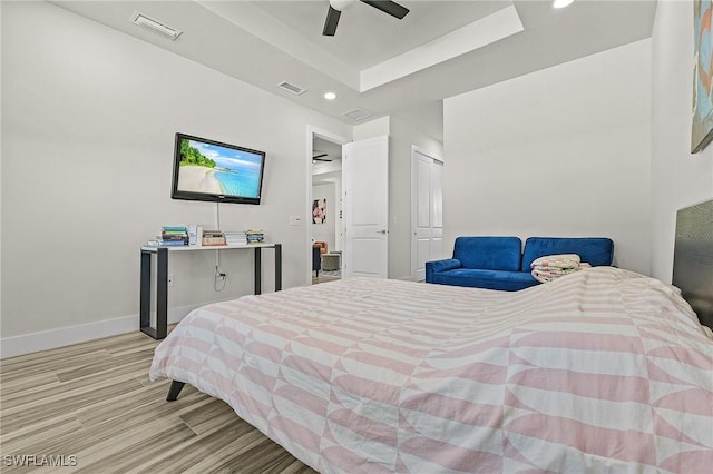 bedroom with ceiling fan, a tray ceiling, and light wood-type flooring