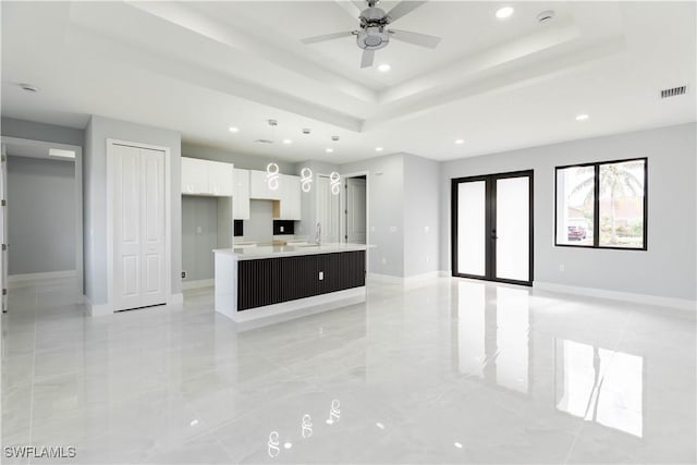 kitchen featuring white cabinetry, ceiling fan, a tray ceiling, a center island with sink, and french doors