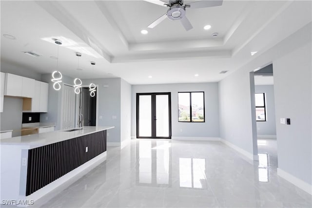 kitchen featuring a tray ceiling, a large island with sink, hanging light fixtures, and white cabinets