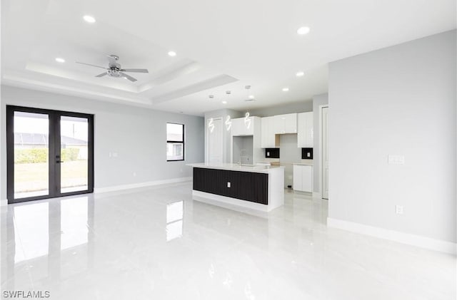 kitchen featuring a raised ceiling, white cabinetry, a wealth of natural light, and a center island with sink