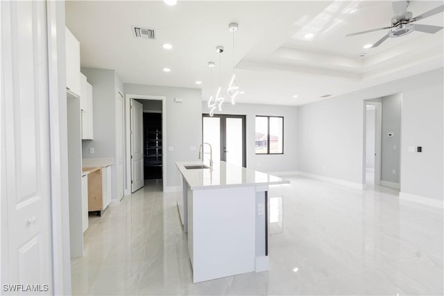 kitchen featuring sink, hanging light fixtures, an island with sink, white cabinets, and a raised ceiling