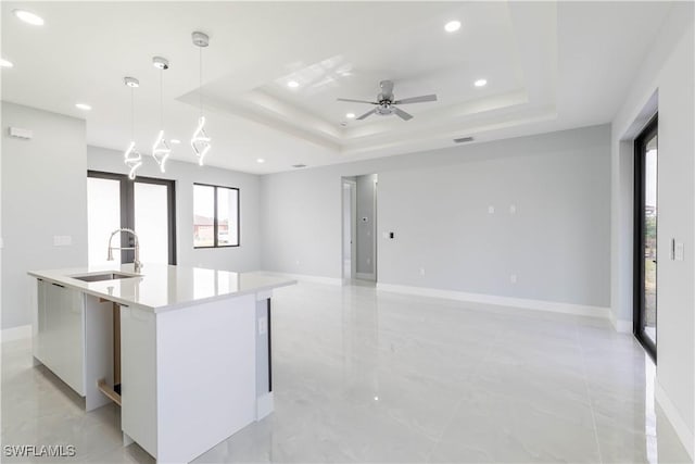 kitchen with a kitchen island with sink, hanging light fixtures, sink, and a raised ceiling