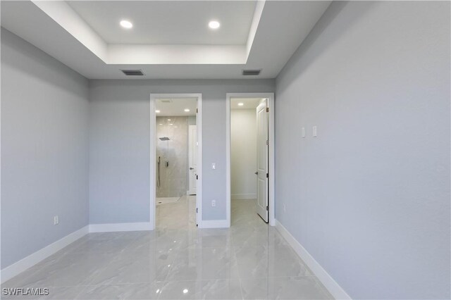 unfurnished bedroom with a raised ceiling, a spacious closet, and connected bathroom