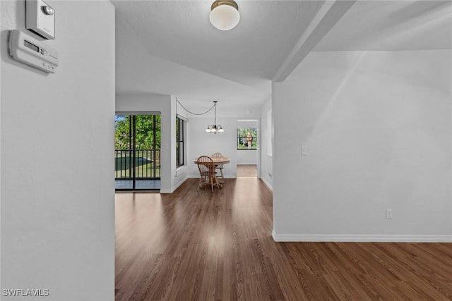 corridor with dark wood-type flooring and an inviting chandelier