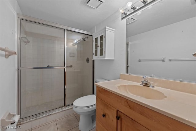 bathroom with tile patterned flooring, vanity, a shower with shower door, and toilet