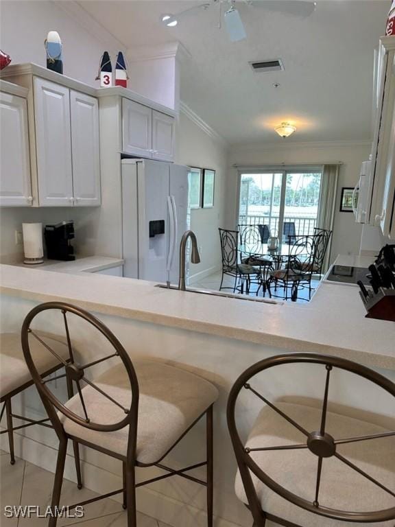 kitchen featuring ornamental molding, white refrigerator with ice dispenser, vaulted ceiling, and kitchen peninsula