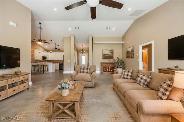 living area with recessed lighting, finished concrete flooring, a warm lit fireplace, and high vaulted ceiling