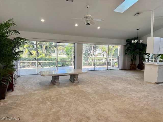 unfurnished living room with vaulted ceiling with skylight, light carpet, and ceiling fan