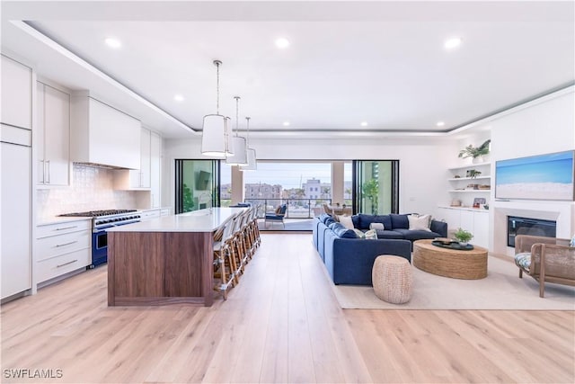 kitchen featuring a kitchen island, white cabinetry, high end range, hanging light fixtures, and light wood-type flooring