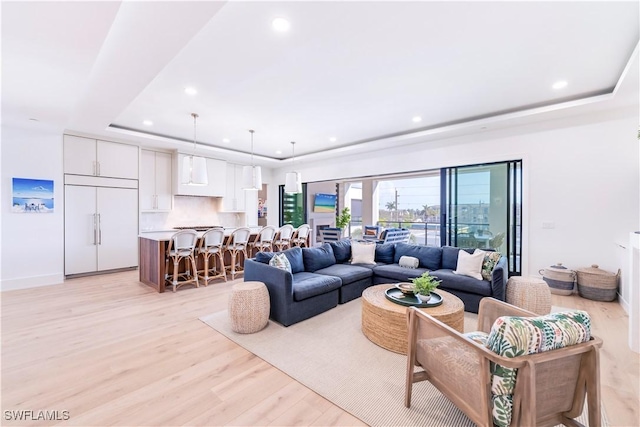 living area with a raised ceiling, recessed lighting, and light wood finished floors