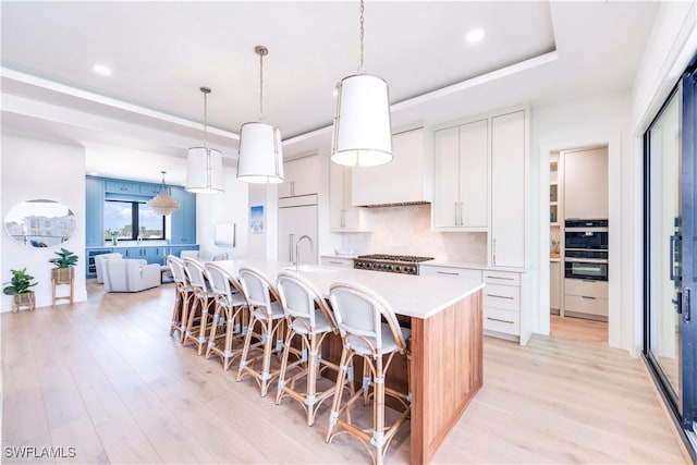 kitchen featuring a tray ceiling, paneled built in fridge, pendant lighting, a kitchen island with sink, and white cabinets