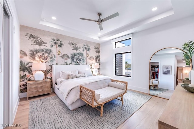 bedroom featuring ceiling fan, a raised ceiling, and light hardwood / wood-style flooring