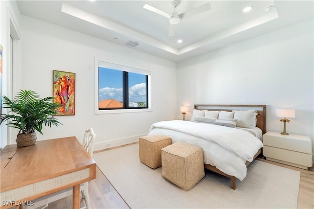 bedroom featuring light hardwood / wood-style flooring, ceiling fan, and a tray ceiling