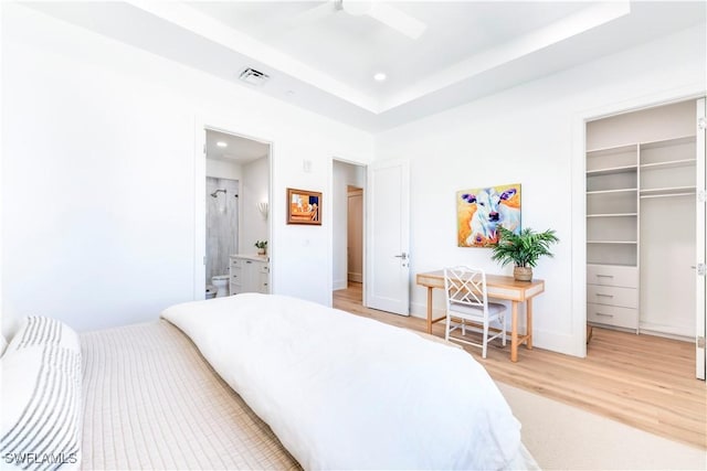 bedroom with ensuite bathroom, hardwood / wood-style flooring, a walk in closet, a tray ceiling, and a closet