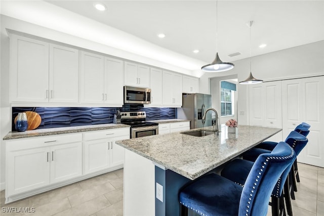 kitchen with sink, hanging light fixtures, stainless steel appliances, light stone countertops, and a center island with sink