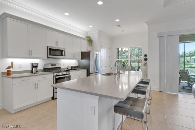 kitchen with appliances with stainless steel finishes, an island with sink, a kitchen breakfast bar, hanging light fixtures, and crown molding