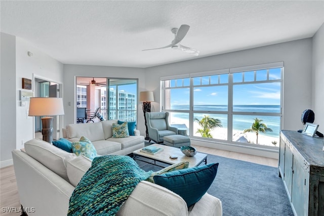 living room with a textured ceiling, light hardwood / wood-style flooring, ceiling fan, and a water view