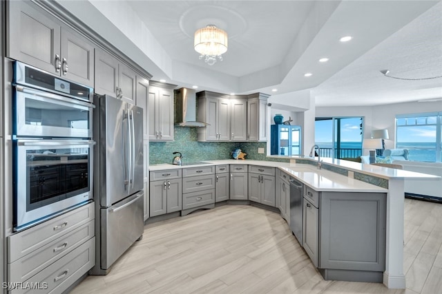 kitchen featuring sink, gray cabinetry, kitchen peninsula, stainless steel appliances, and wall chimney range hood