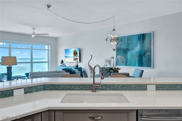 kitchen featuring ceiling fan with notable chandelier, decorative light fixtures, dishwasher, sink, and a textured ceiling