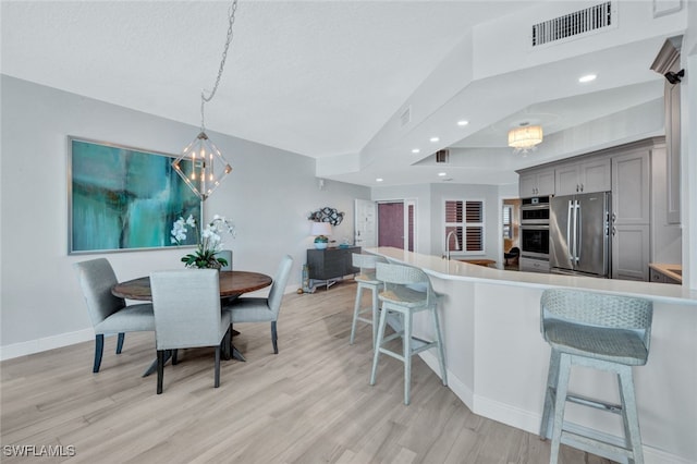 kitchen featuring gray cabinetry, hanging light fixtures, stainless steel appliances, a kitchen breakfast bar, and light hardwood / wood-style floors