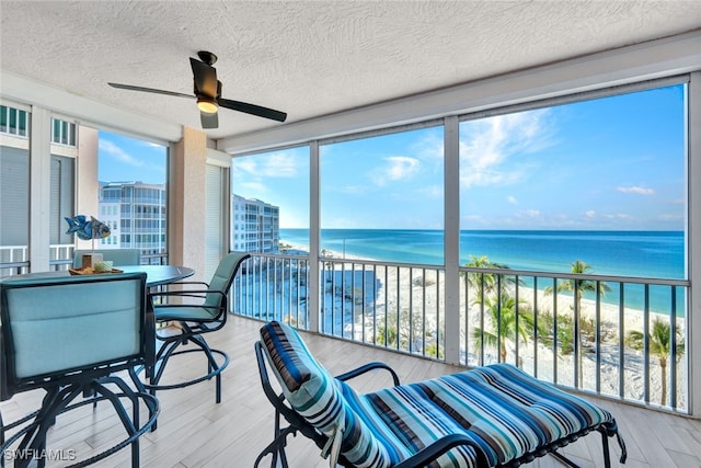 sunroom / solarium featuring a water view, ceiling fan, and a beach view