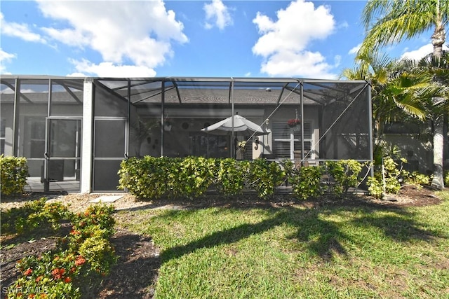 rear view of property featuring a yard and glass enclosure