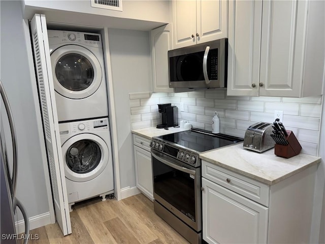 kitchen with tasteful backsplash, white cabinets, stacked washer and clothes dryer, stainless steel appliances, and light hardwood / wood-style flooring