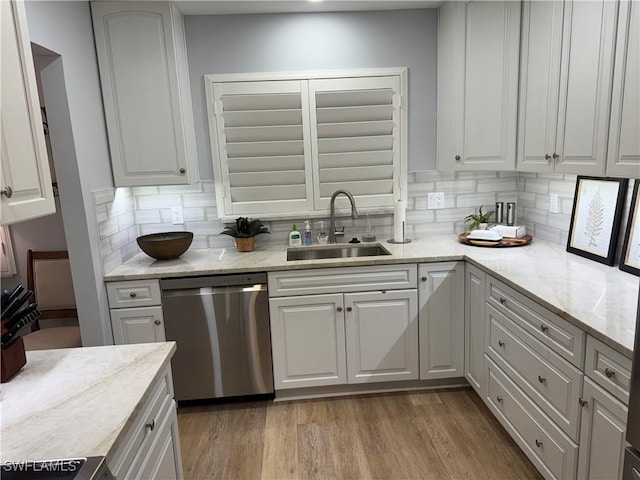 kitchen featuring white cabinetry, sink, stainless steel dishwasher, light stone countertops, and light hardwood / wood-style flooring