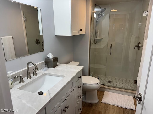 bathroom featuring hardwood / wood-style flooring, vanity, a shower with shower door, and toilet