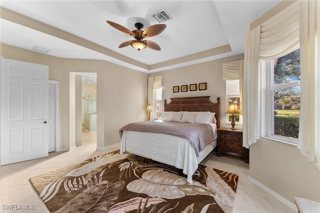 bedroom with ensuite bathroom, a tray ceiling, multiple windows, and light tile patterned floors