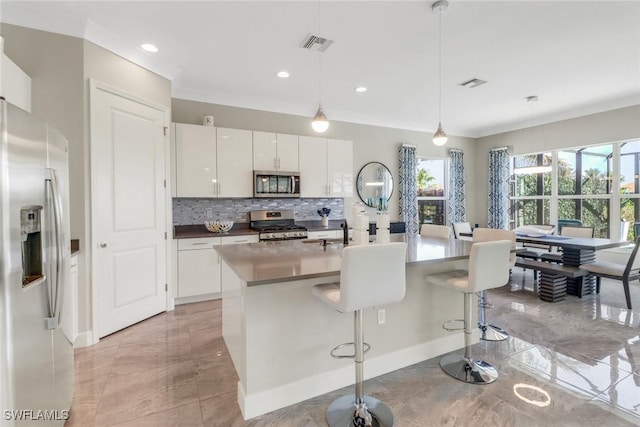 kitchen featuring white cabinets, a kitchen breakfast bar, hanging light fixtures, stainless steel appliances, and a center island with sink